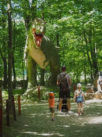Rodzina zwiedzająca park dinozaurów z wielką figurą T-Rexa w Zatorlandzie.