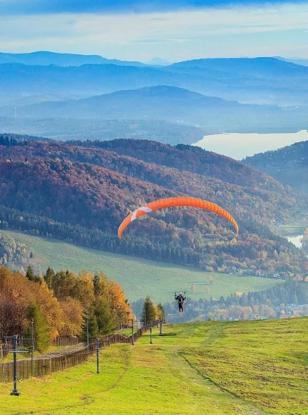 Czerwony wagonik kolei linowo-terenowej na Górze Żar z panoramą Jeziora Międzybrodzkiego.