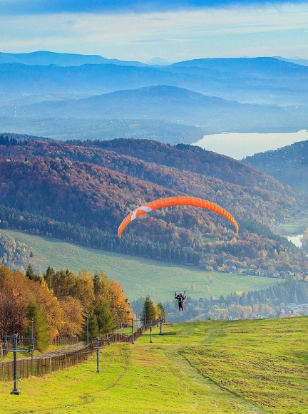 Czerwony wagonik kolei linowo-terenowej na Górze Żar z panoramą Jeziora Międzybrodzkiego w tle.