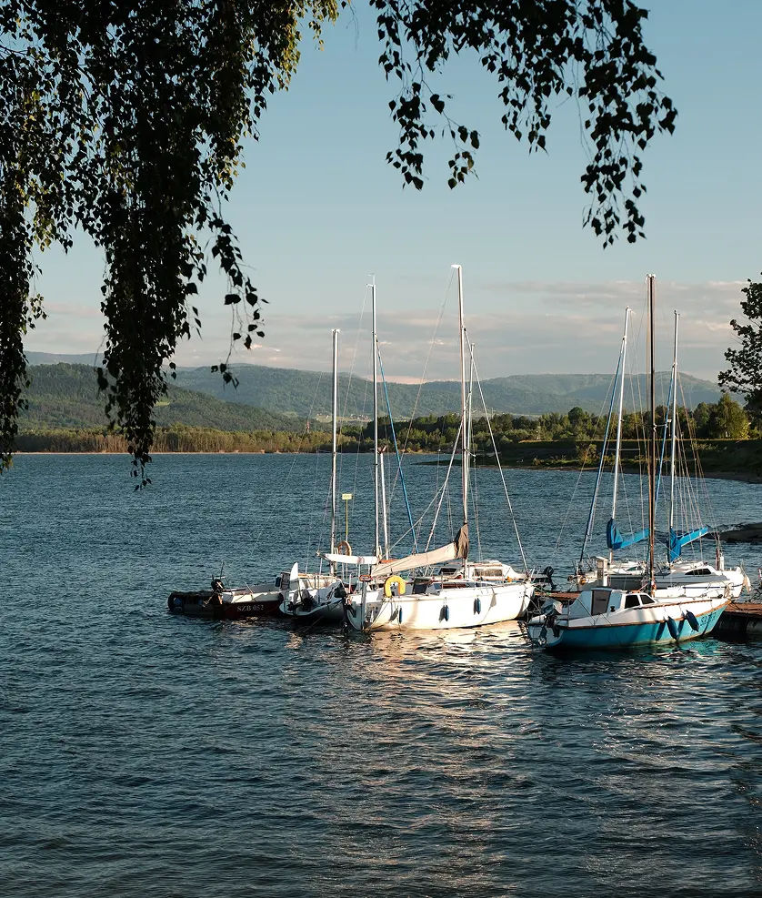 Żaglówki zacumowane w marinie na Jeziorze Żywieckim z panoramą Beskidów w tle – otoczenie inwestycji TREESNA Kombi Invest