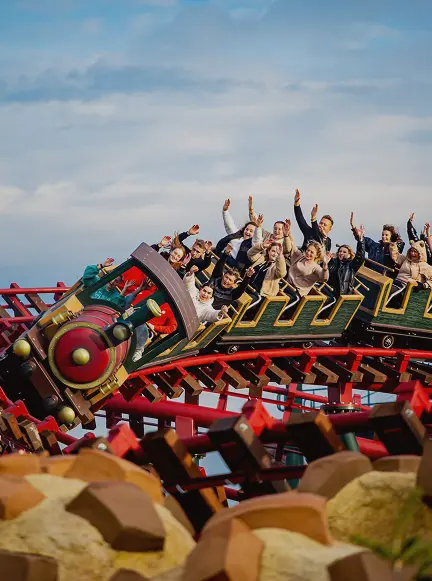 Grupa osób jadąca rollercoasterem w Energylandii, unosząca ręce podczas zjazdu – atrakcja dla mieszkańców TREESNA Kombi Invest