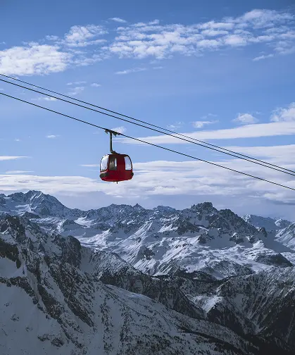 Czerwona gondola kolejki linowej unosząca się nad ośnieżonymi szczytami – zimowe atrakcje w pobliżu TREESNA Kombi Invest