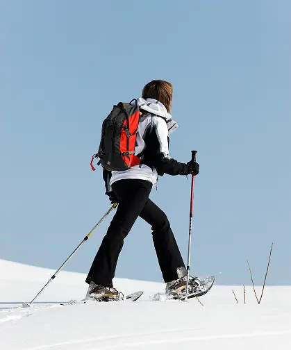 Kobieta w zimowym stroju idąca na rakietach śnieżnych po świeżym śniegu – zimowa aktywność w pobliżu TREESNA Kombi Invest