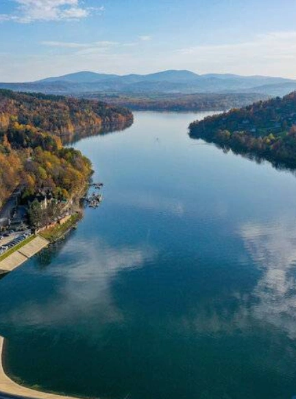 Kilka żaglówek pływających po Jeziorze Żywieckim w słoneczny dzień, w tle widoczny szczyt góry Żar.