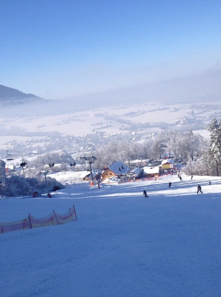 Sześcioosobowa kanapa wyciągu narciarskiego w ośrodku Czarny Groń nad ośnieżonym stokiem z narciarzami.
